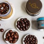 Satori cannabis-infused CBD blueberries in dark chocolate, shown in tins and small white dishes on a gray surface.