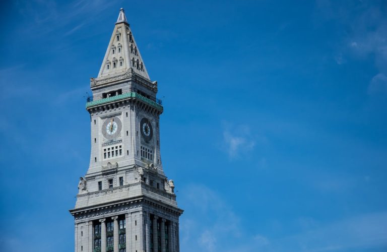 Boston Custom House Tower clock tower rising against a clear blue sky, featuring ornate stonework and a pointed spire.